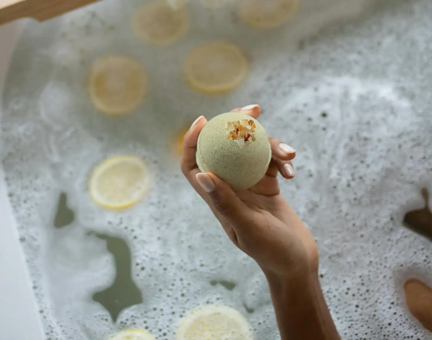 Weibliche Hand hält eine Badekugel über eine volle Badewanne